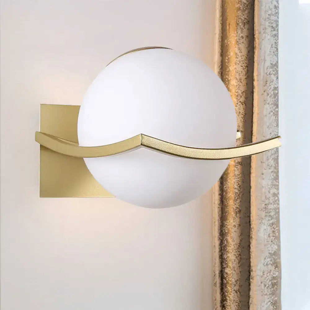 A modern black and gold wall sconce with a frosted opal glass globe shade, ideal for bedroom LED lighting