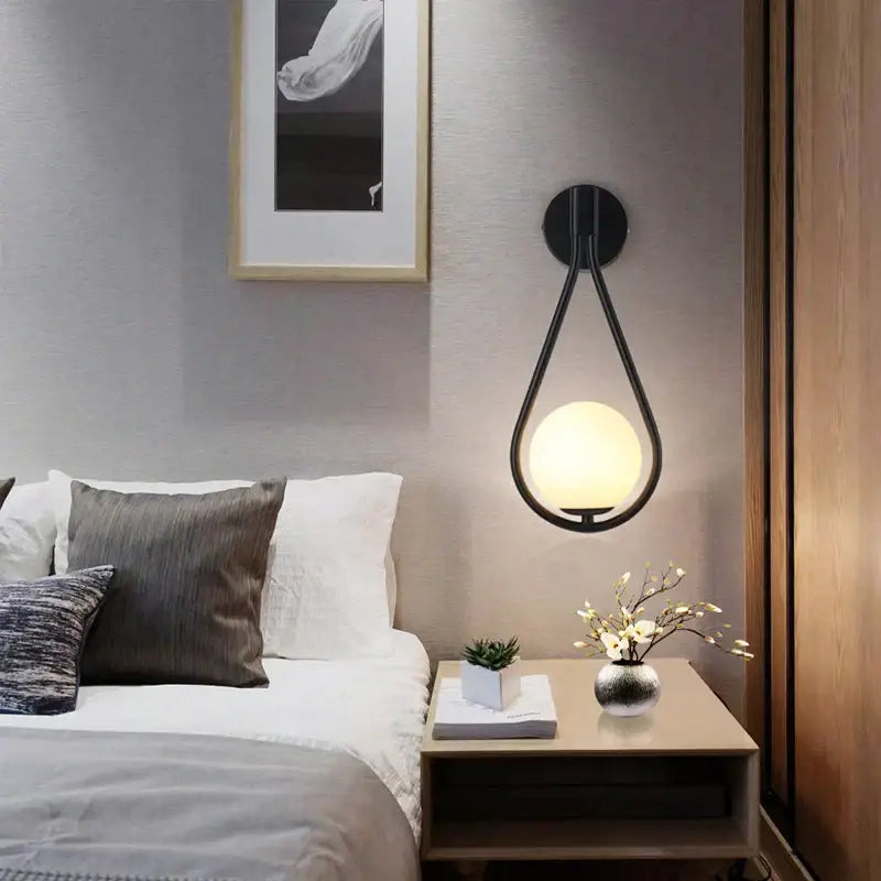 Modern black and gold teardrop led wall sconce with glass globe light featuring a glowing spherical bulb for bedroom use