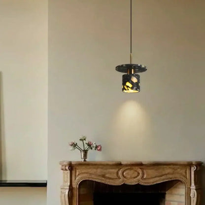 A sleek modern black and gold terrazzo stone pendant lamp with mosaic design hangs above an ornate wooden mantel