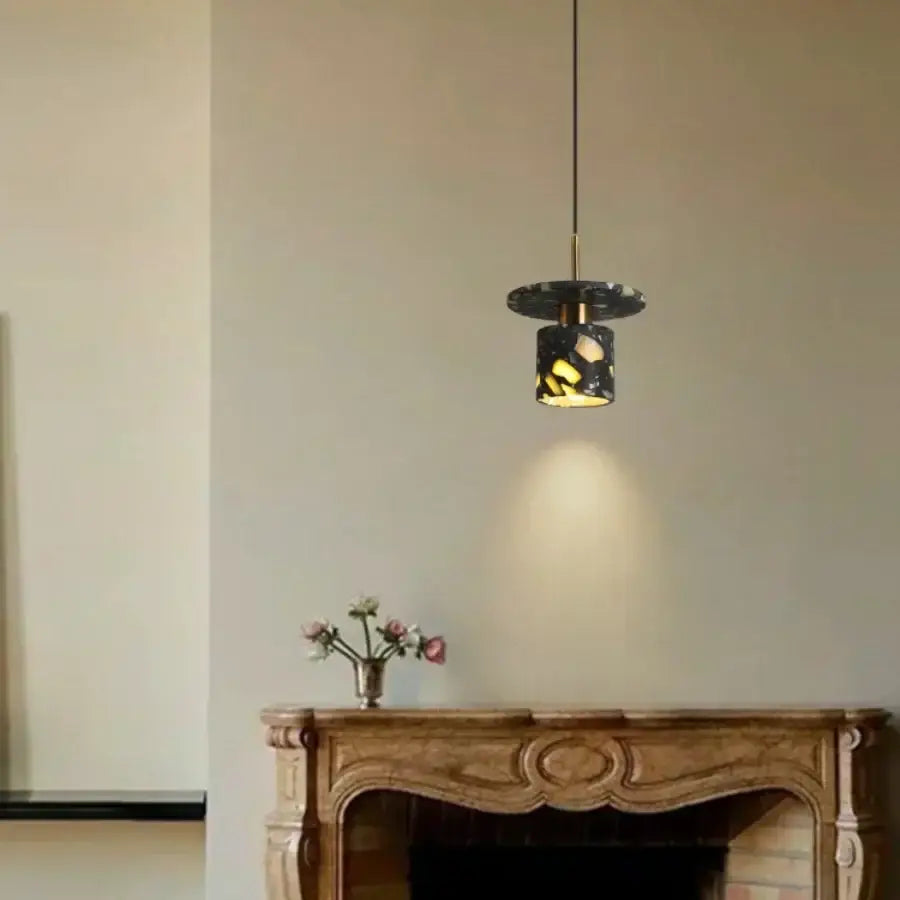 A sleek modern black and gold terrazzo stone pendant lamp with mosaic design hangs above an ornate wooden mantel
