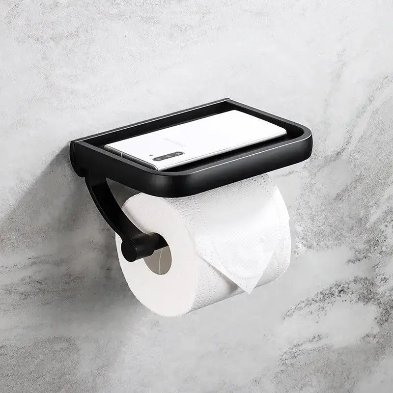 Black metal tissue paper holder with integrated phone tray holding a white smartphone for bathroom use