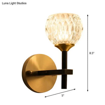 Gold-toned wall light with faceted dimpled glass shade and black metal arm for living room illumination