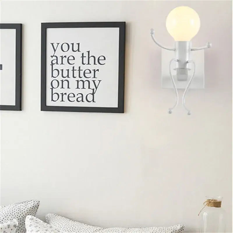 White whimsical wall sconce with articulated arms and legs holding a bulb decorbites cartoon doll wall sconce for kids bedroom