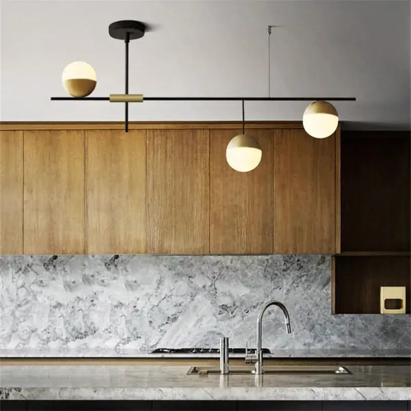 Modern black linear chandelier with brass decorbites glass ball shades featuring three glowing orbs above kitchen counter