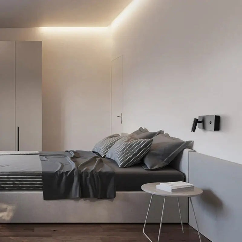Minimalist white bedside table with slender metal legs beside a modern black matte led wall sconce for reading light