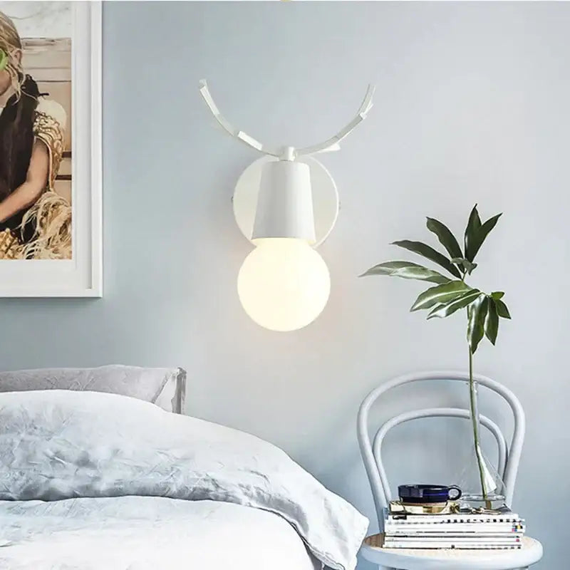 White antler-shaped wall lamp featuring a frosted globe bulb and black metal deer head led design for bedroom decor