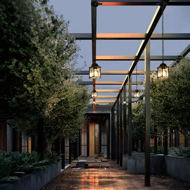 Modern black metal lantern courtyard pendant light with warm glowing glass panels hanging from a pergola pendant lamp decorbites garden pendant