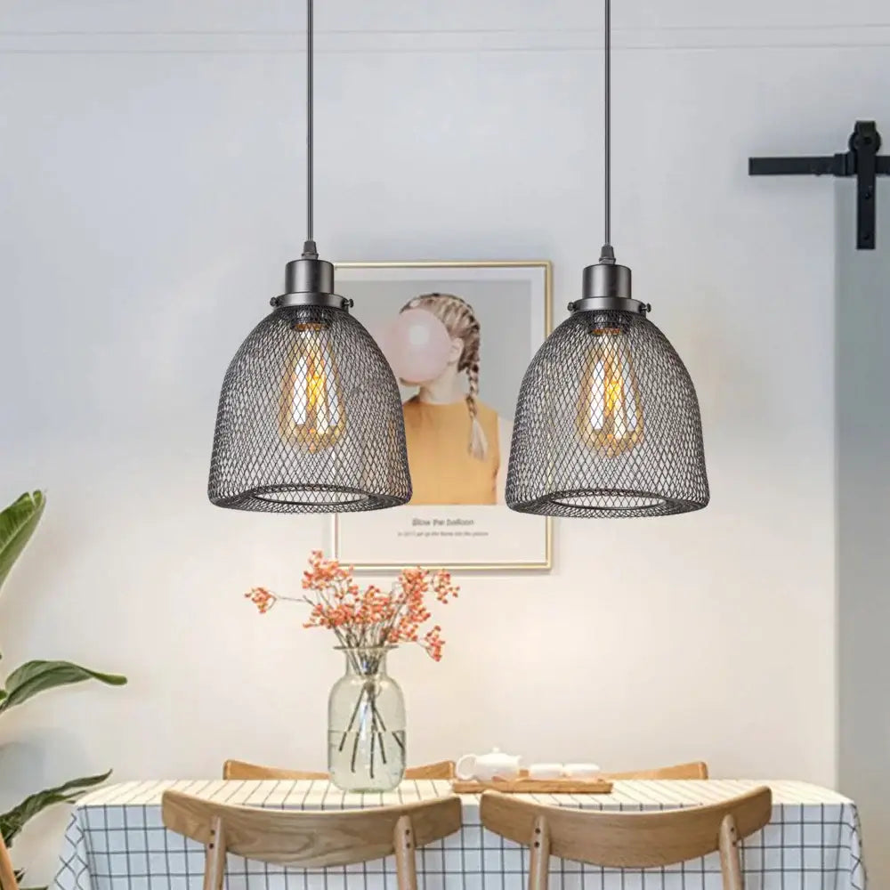 Two black metal mesh pendant light chandeliers with exposed filament bulbs hang above a dining room table