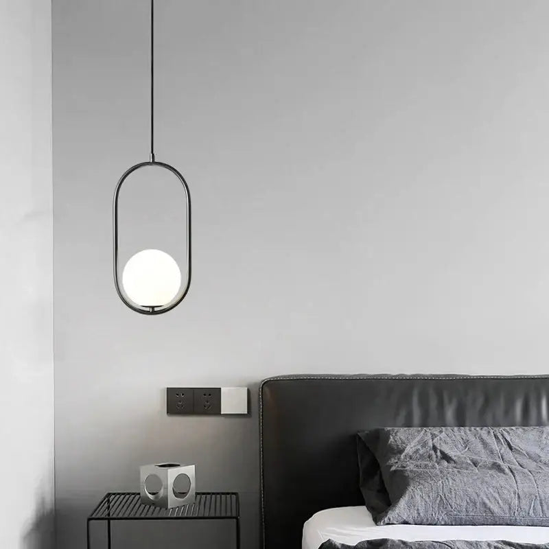 Modern black metal ring pendant light with a sleek oval frame and glowing white glass globe shade for dining room