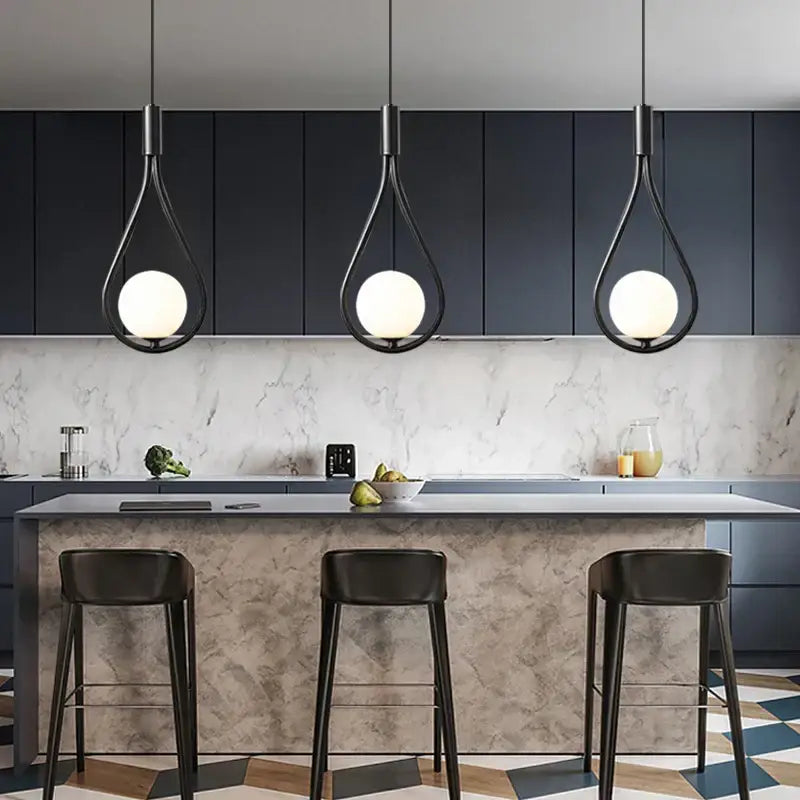 Three sleek black metal pendant lights with frosted glass globes hang above a modern kitchen island