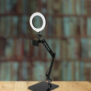 Black adjustable ring light with metal shade and smartphone mount on articulated arm for bedroom use