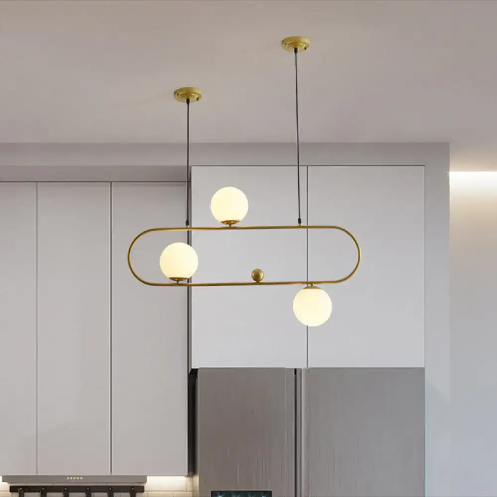 Gold-toned modern minimalist ellipse ceiling light with three frosted glass globes hanging by black cords for living room use