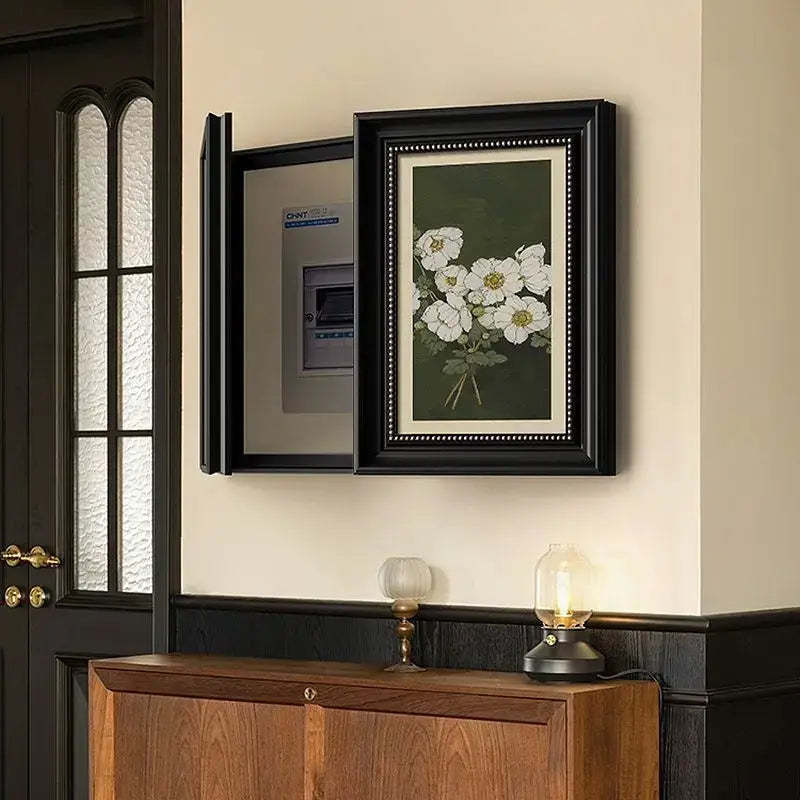 Black-framed decorative painting with white flowers on dark green for modern electric meter box cover above wooden cabinet