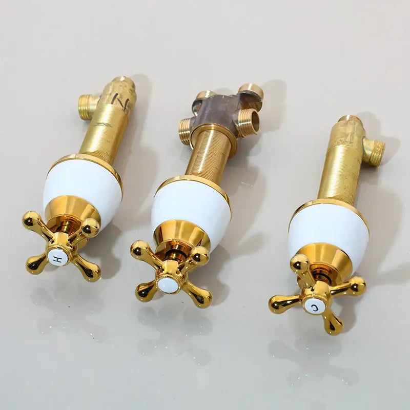 Three gold-finished bathroom water control valve faucets with white ceramic handles and black painting details
