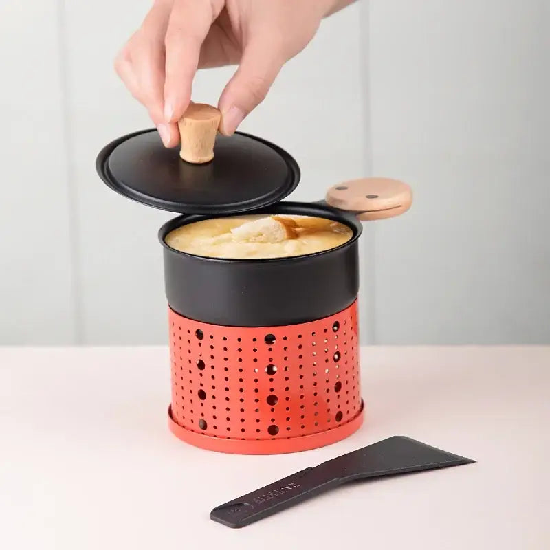 Modern black raclette fondue set with an orange perforated metal pot black lid wooden knob and side handle for easy use