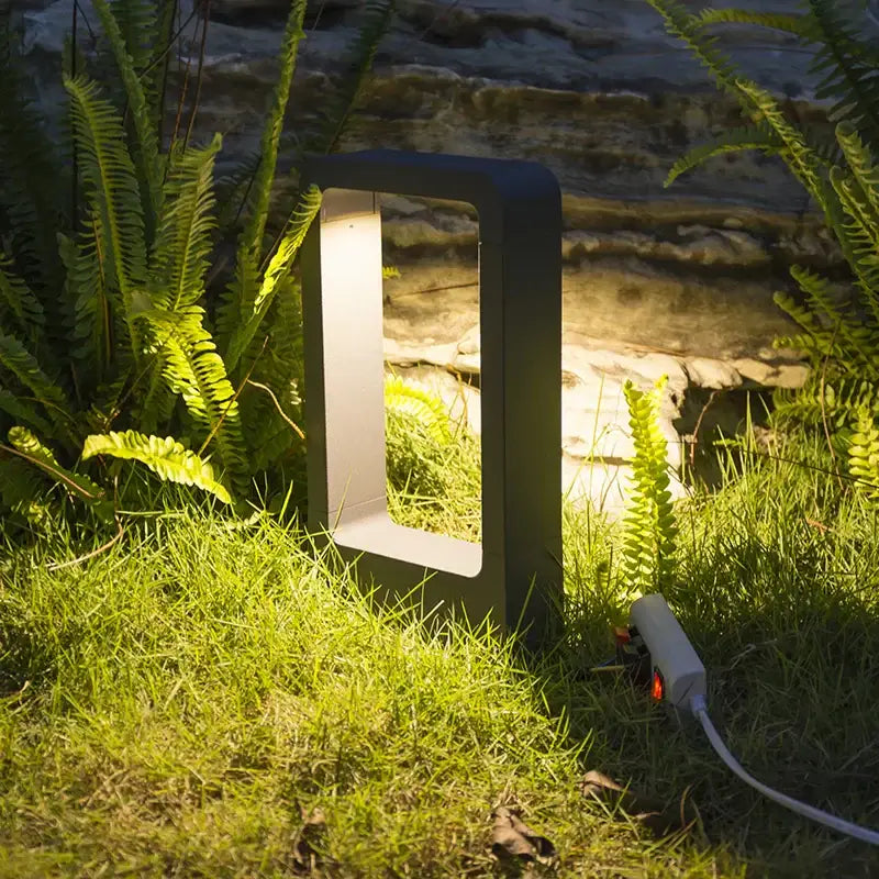 Modern black rectangular led lawn light with glowing white interior casting warm light on grass and ferns