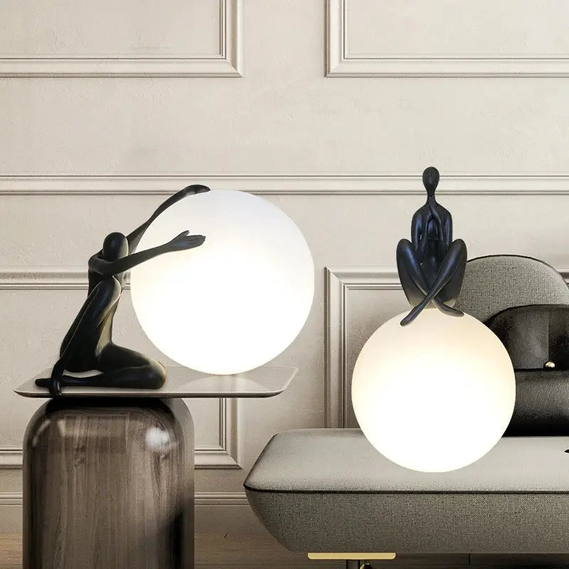 Two matte black minimalist table lamps with sculptural figures atop glowing white glass ball holders for decorbites abstract humanoid decor