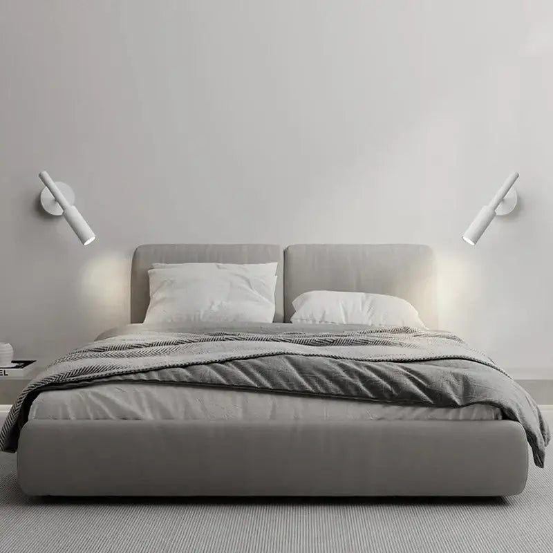Modern black rotatable led wall lamp illuminating a gray upholstered bed with matching headboard and footboard in bedroom