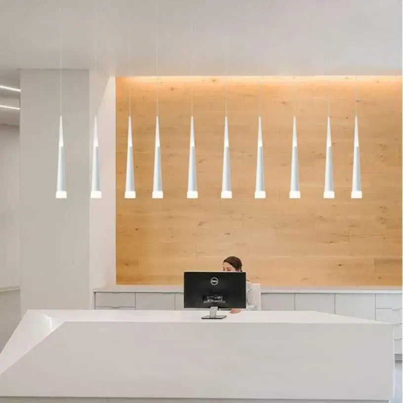 Modern white conical pendant lights hanging above a reception desk in black and silver decorbites conical tube style