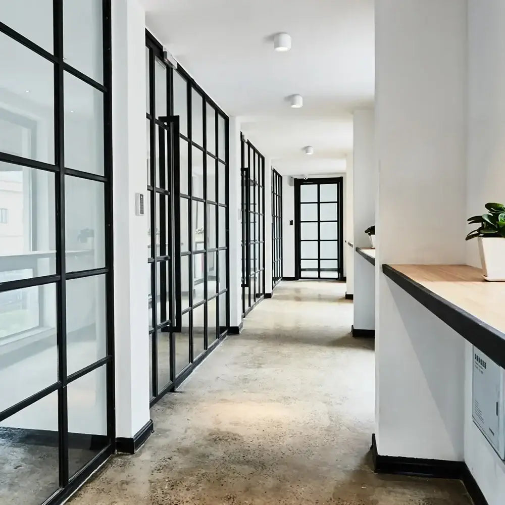 Modern black surface mount ceiling light installed in a hallway with black framed glass partition walls