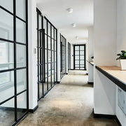 Modern black surface mount ceiling light installed in a hallway with black framed glass partition walls