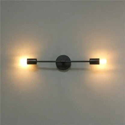 Modern black two arm led wall lamp with cylindrical fixtures emitting warm glow for bedroom vanity use