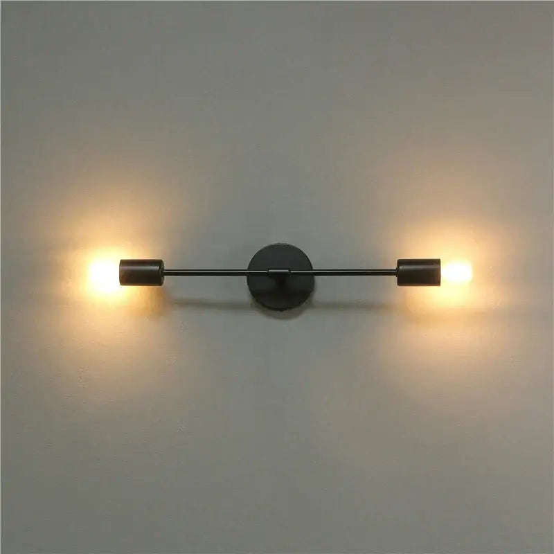 Modern black two arm led wall lamp with cylindrical fixtures emitting warm glow for bedroom vanity use