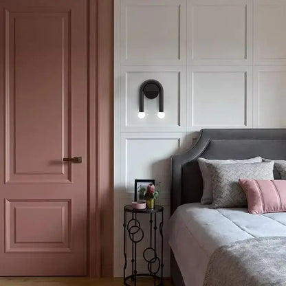 Modern black u-shape led wall lamp with spherical bulbs mounted above gray upholstered bed with pink patterned pillows