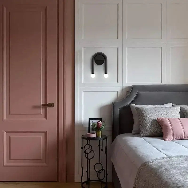 Modern black u-shaped led wall lamp with spherical bulbs above gray upholstered bed with patterned and solid pink pillows