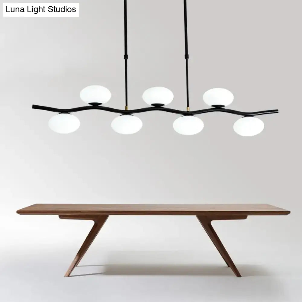 Modern black wavy pendant light with five white glass globes suspended above a wooden dining table by DecorBites