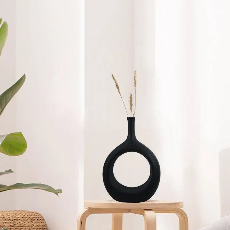 Modern black decorbites ceramic vase with circular cutout and slender neck holding dried wheat for living room decor