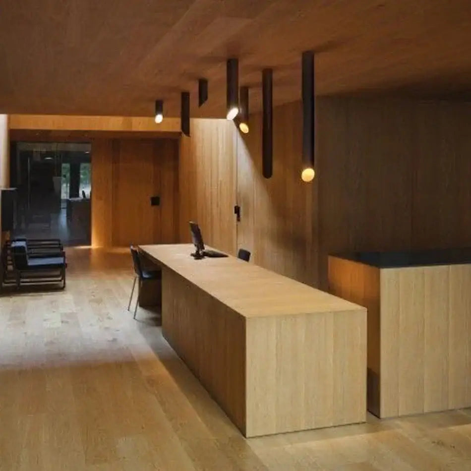 Modern black and white cylindrical led ceiling light above a long wooden reception desk with natural wood grain finish