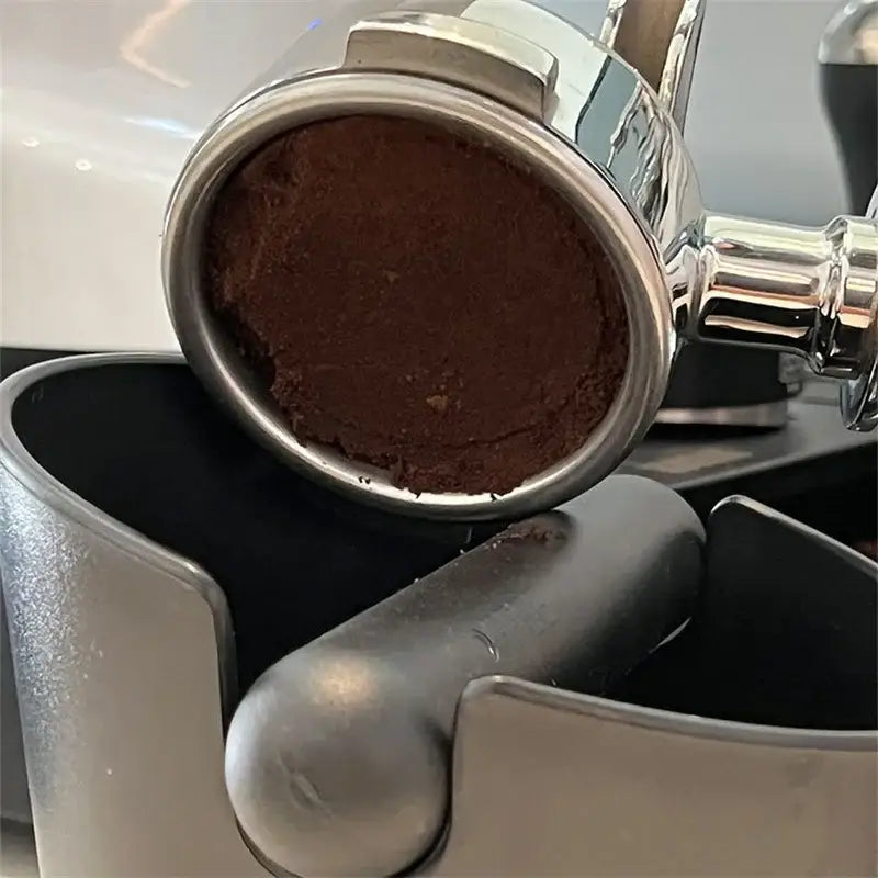 A shiny stainless steel espresso portafilter with dark ground coffee in a modern black and white decorbites espresso knock box