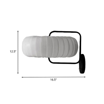 A modern black and white gathered fabric pumpkin wall sconce with a white ribbed glass lamp and black metal frame