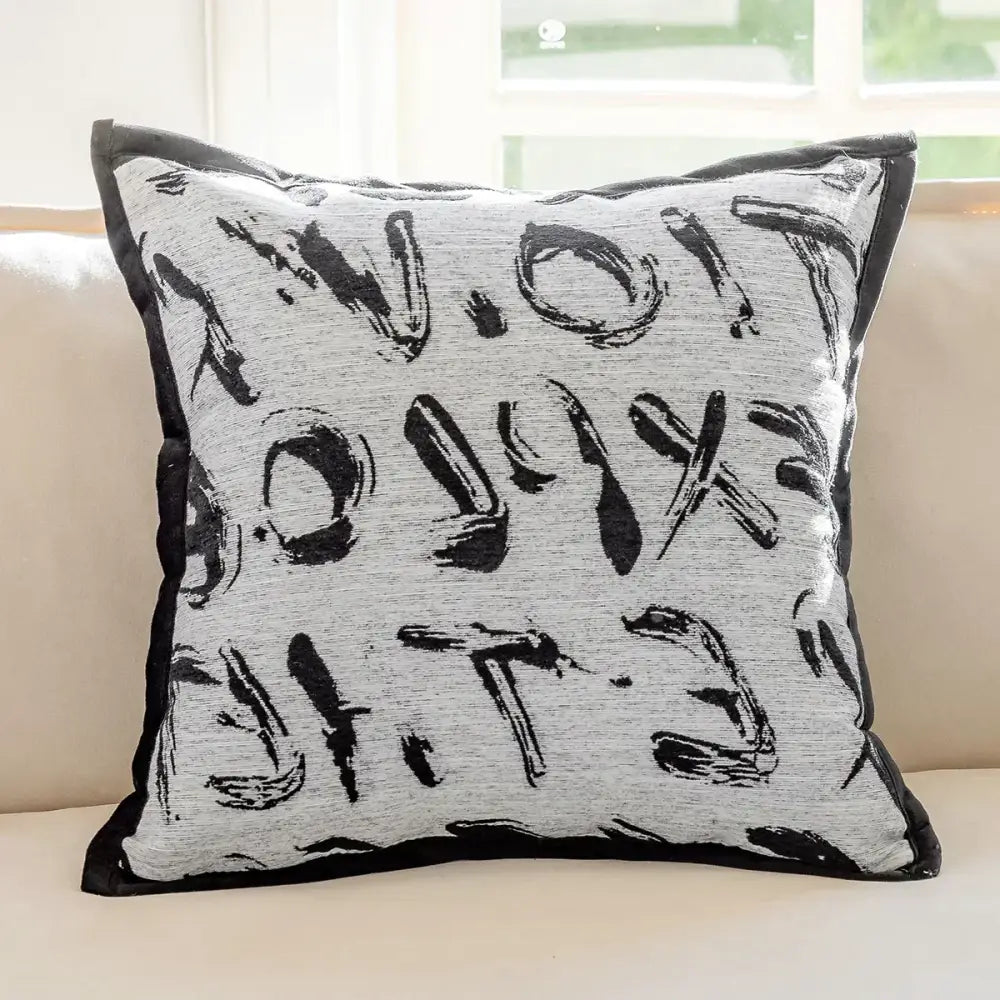 A modern black and white geometric jacquard cushion cover with gray fabric, bold black brushstroke lettering, and a black velvet border
