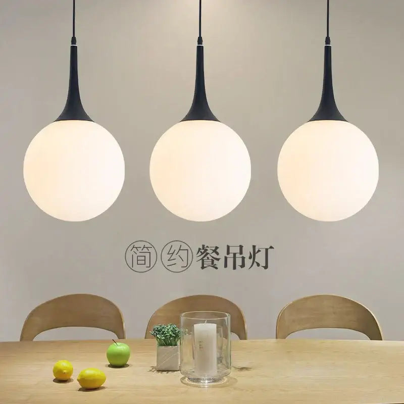 Three black pendant lights with spherical frosted glass shades hang above a wooden table decorbites glass ball led