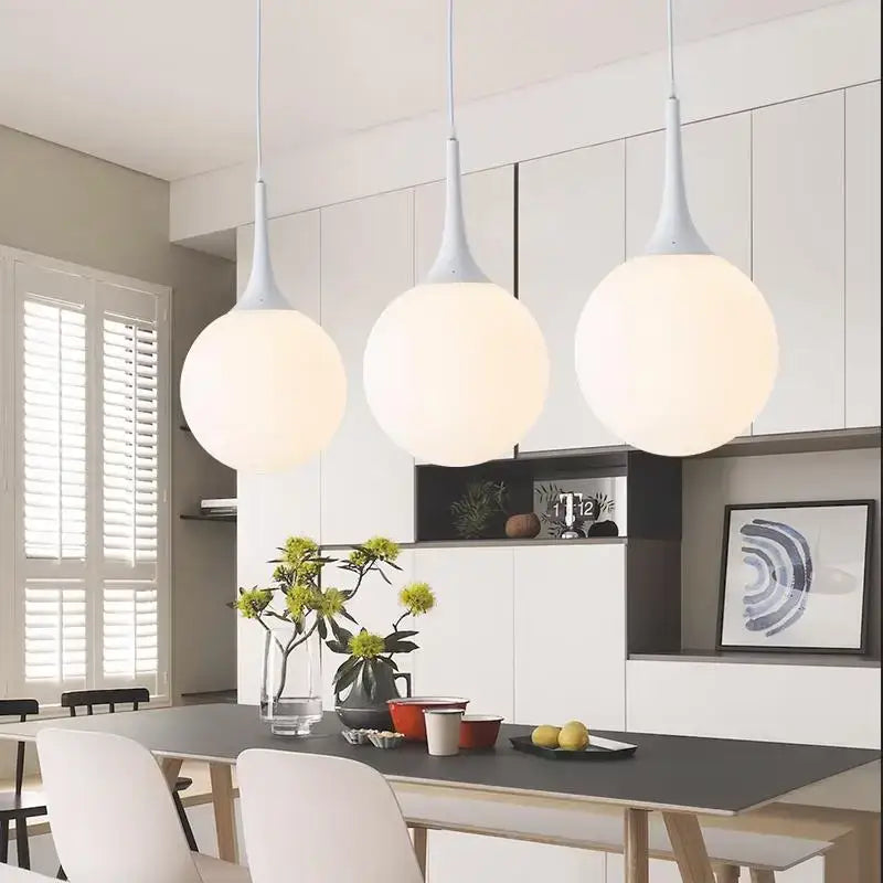 Three modern decorbites glass ball pendant lamps with white frosted globes and matte gray stems above dining table