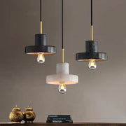 Three modern pendant lights with black and white matte shades, gold accents, and decorbites green marble details