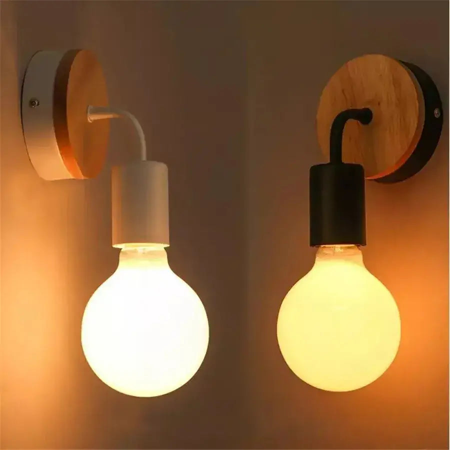 Two modern black and white iron art wall light sconces with round wooden backplates and exposed globe bulbs by decorbites