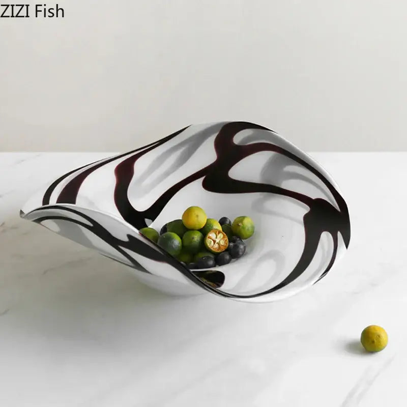 A modern black and white marbled glass fruit plate with abstract swirls holds green limes and dark berries