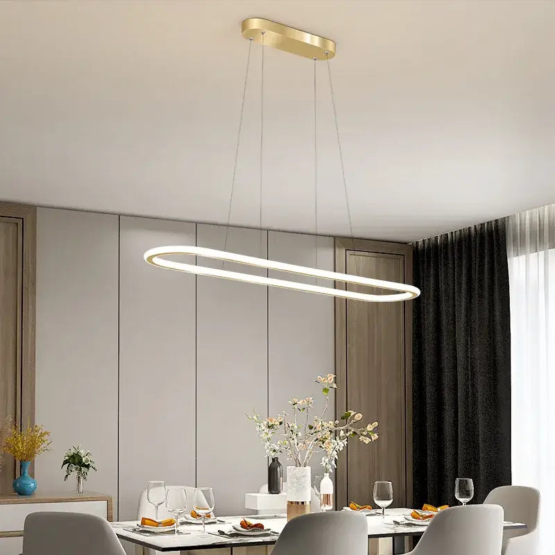 Modern gold-finished oval led chandelier with sleek minimalist design hanging above dining table for modern interiors