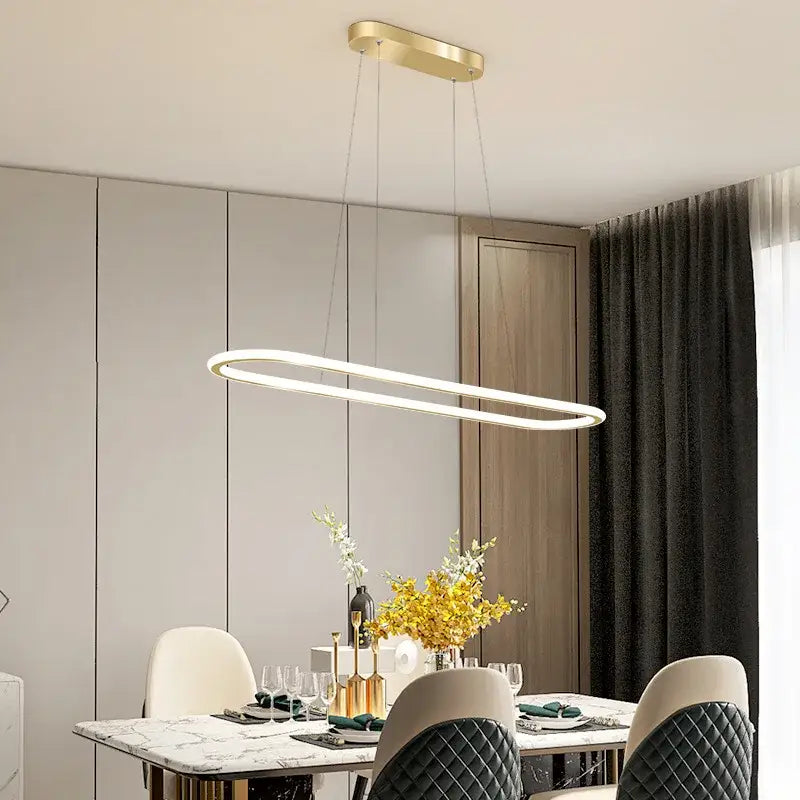 Modern gold-toned oval led chandelier with sleek minimalist design hanging above dining table for ambient lighting