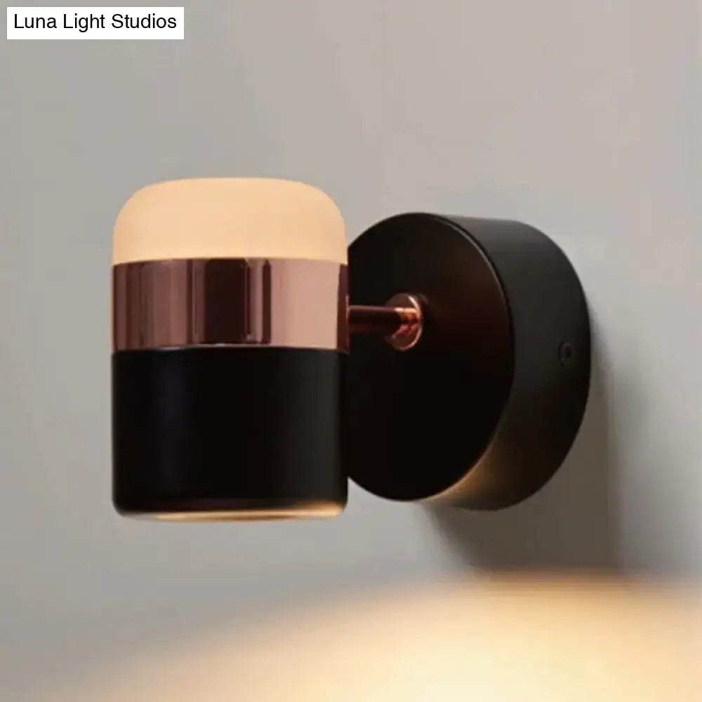 Modern black and white bedroom wall sconce with matte black cylindrical body, rose gold band, and frosted glass diffuser