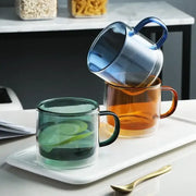 Modern blue amber and green glass mugs set featuring three translucent glass mugs with matching colored handles on a tray