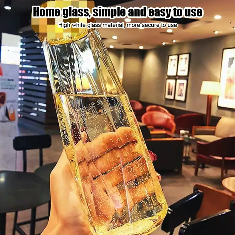 A clear high white glass diamond water bottle with faceted design and gold-toned cap for kitchen and sport travel