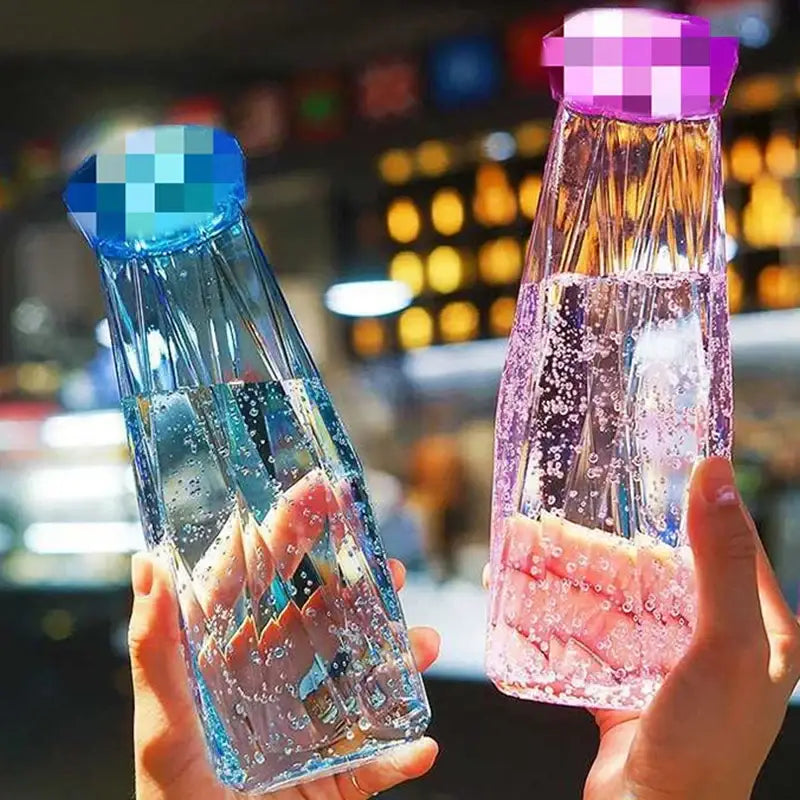Two translucent faceted diamond water bottles with blue and purple lids filled with sparkling water for kitchen and travel