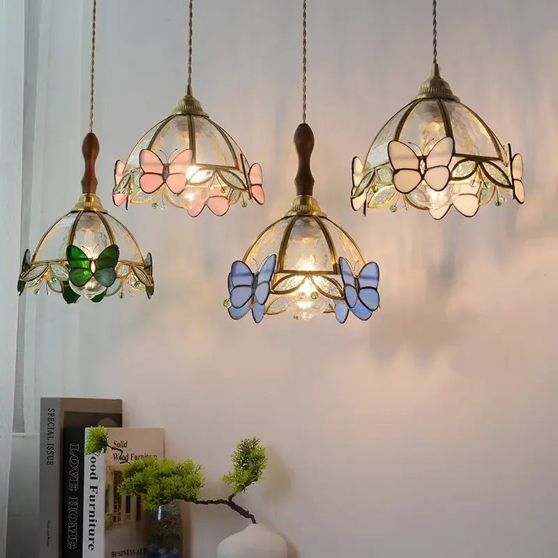 Three hanging dome-shaped decorbites butterfly glass led pendant lights in pastel hues framed by brass metalwork for kitchen decor