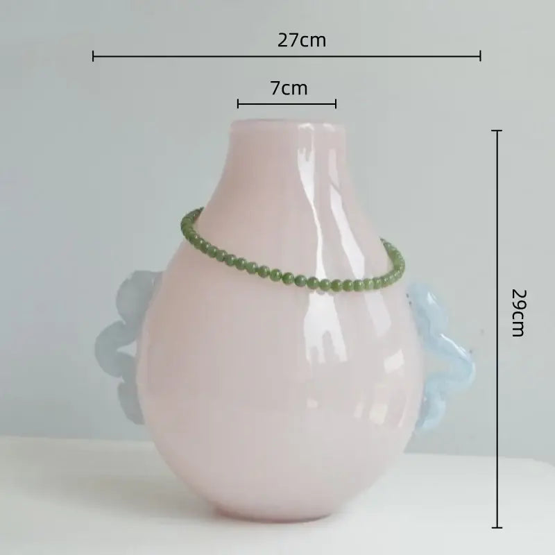 A blush pink ceramic vase with light blue handles and green beads paired with modern glass geometric flower decor