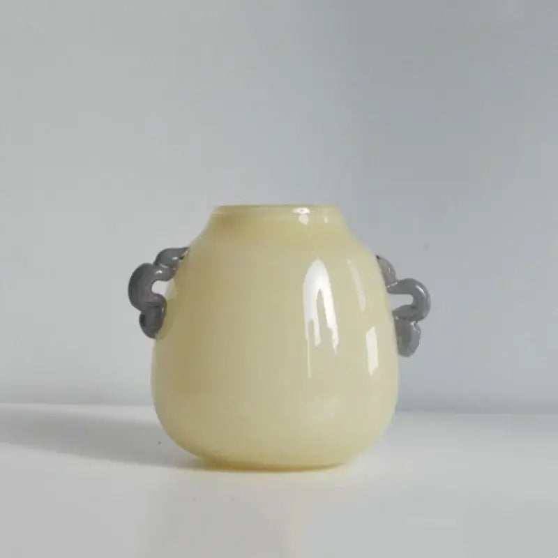 A smooth pale yellow ceramic vase with dark gray carved handles paired with a modern blue and orange glass geometric flower vase