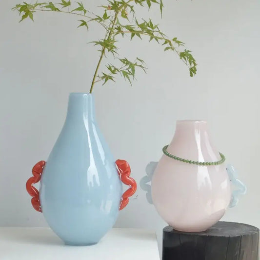 A sleek light blue glass geometric flower vase with vibrant orange sculpted handles for modern living room decor